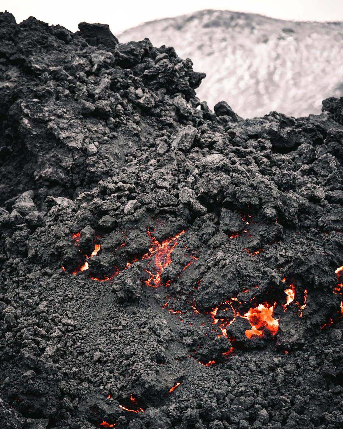 La lava fusa scorre attraverso crepe in rocce vulcaniche scure e frastagliate.