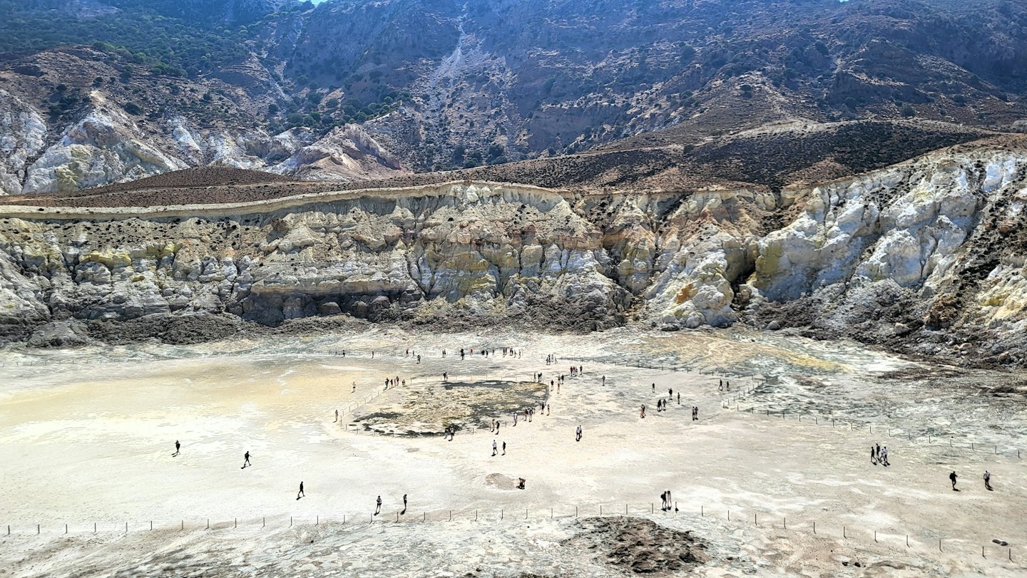 Persone esplorano il suolo roccioso di una vasta caldera vulcanica.