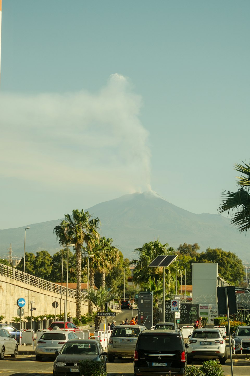 Un vulcano fumante incombe su una strada urbana trafficata.